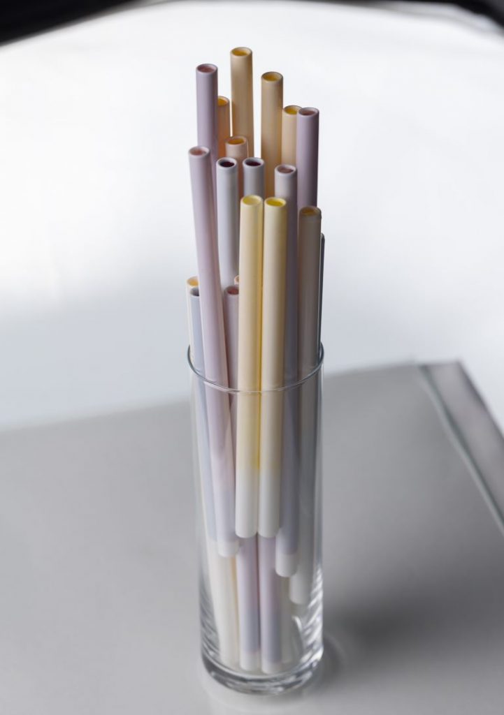 Straws with different flavors in a glass that is standing on a flat surface.