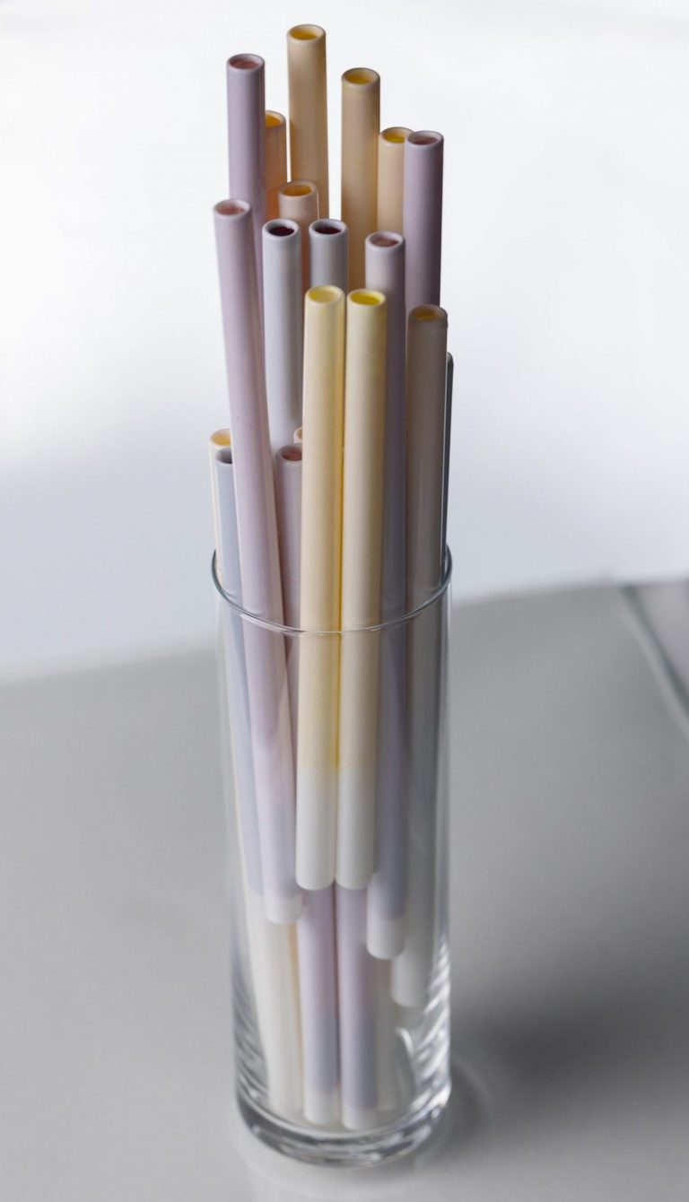 Straws with different flavors in a glass that is standing on a flat surface.